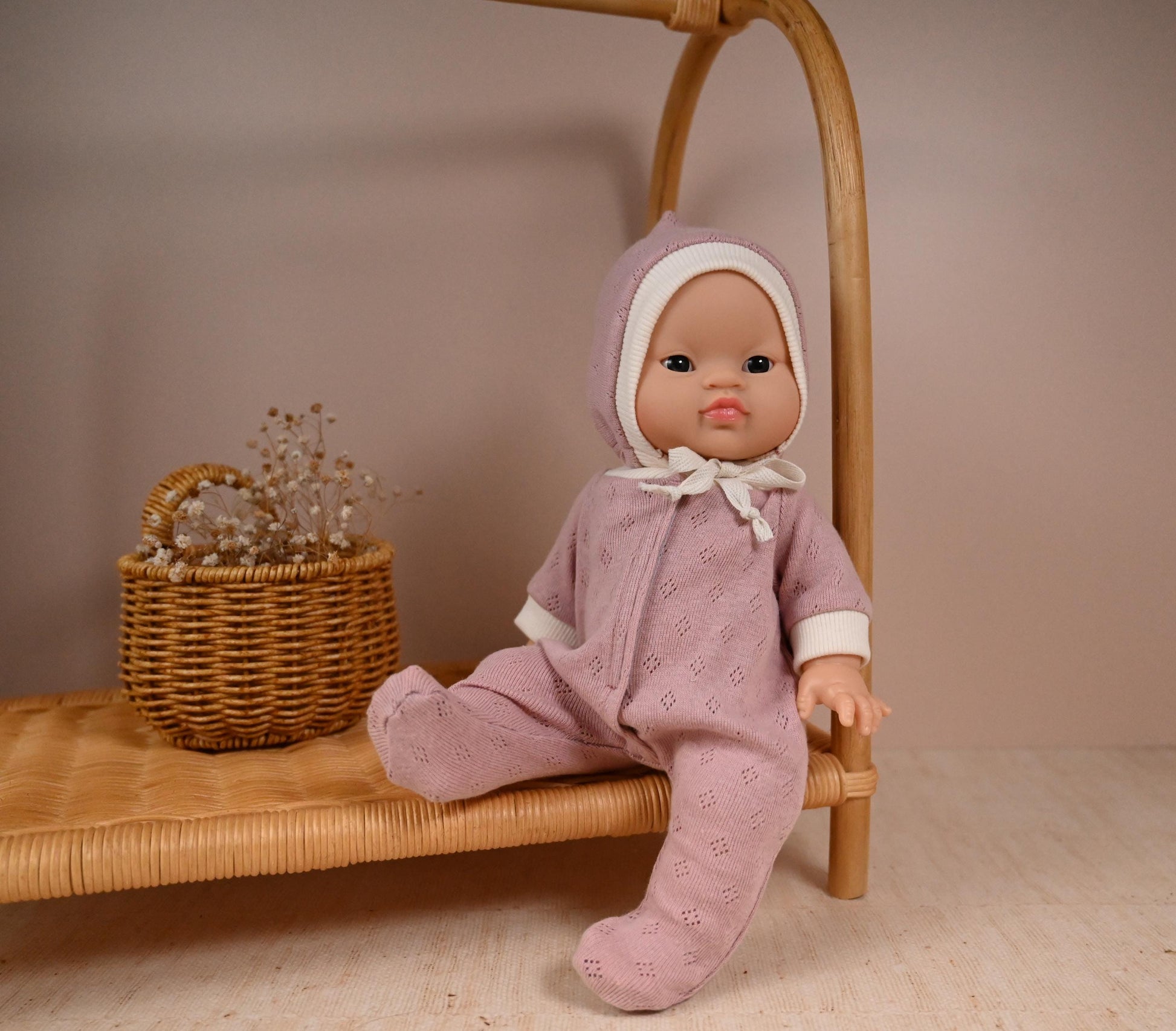 his cosy footed sleeper is made from soft, breathable cotton jersey in a beautiful dusty rose shade — perfect for keeping your doll snug and stylish.

The delicate eyelet knit pattern adds a vintage-inspired charm, while the ribbed cuffs and matching bonnet complete the look with comfort and care. Thoughtfully designed to fit 34cm dolls like Minikane and Paola Reina, it’s ideal for bedtime play and quiet cuddles.
Handmade from&nbsp; 100% Pointelle Cotton Jersey