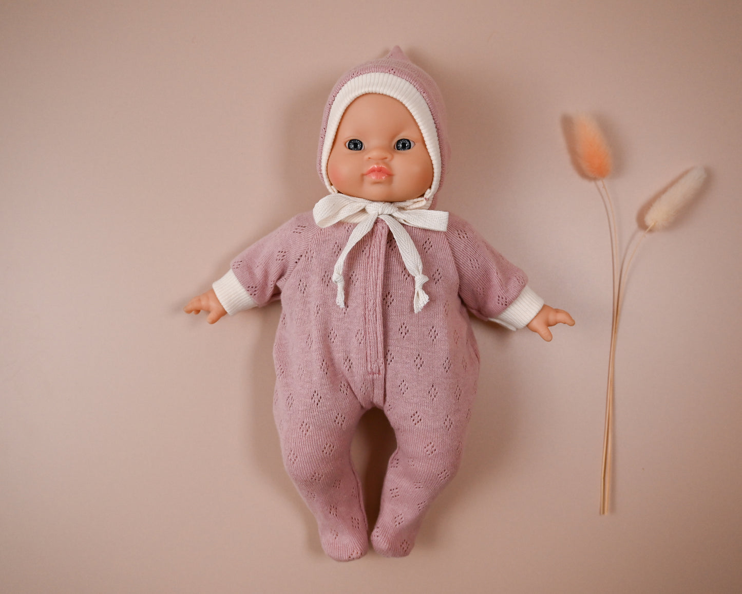 Handmade from Soft Cotton Jersey
This cosy footed sleeper is made from soft, breathable cotton jersey in a beautiful dusty rose shade — perfect for keeping your doll snug and stylish.

The delicate eyelet knit pattern adds a vintage-inspired charm, while the ribbed cuffs and matching bonnet complete the look with comfort and care. Thoughtfully designed to fit 28cm dolls like Minikane, it’s ideal for bedtime play and quiet cuddles.