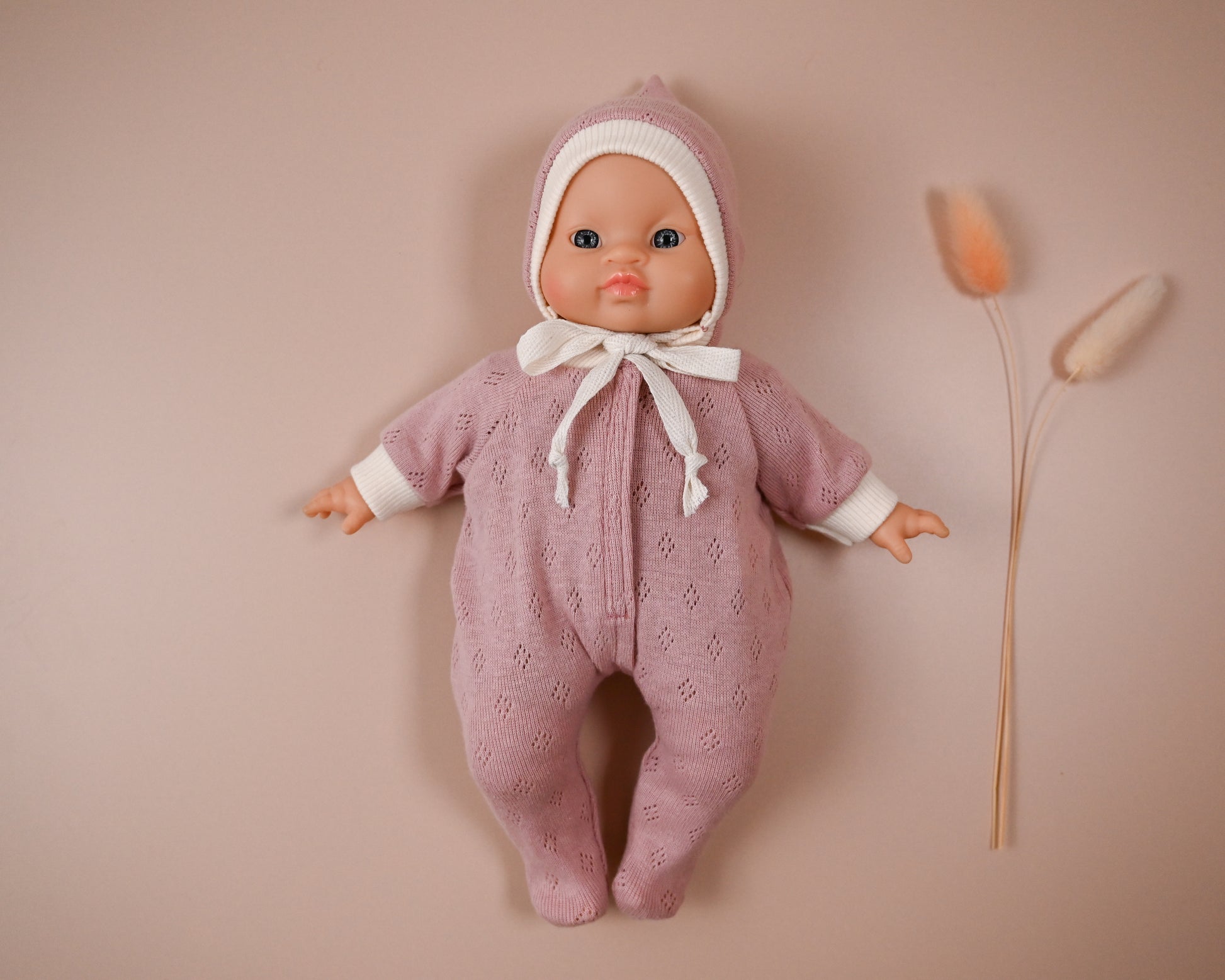 Handmade from Soft Cotton Jersey
This cosy footed sleeper is made from soft, breathable cotton jersey in a beautiful dusty rose shade — perfect for keeping your doll snug and stylish.

The delicate eyelet knit pattern adds a vintage-inspired charm, while the ribbed cuffs and matching bonnet complete the look with comfort and care. Thoughtfully designed to fit 28cm dolls like Minikane, it’s ideal for bedtime play and quiet cuddles.