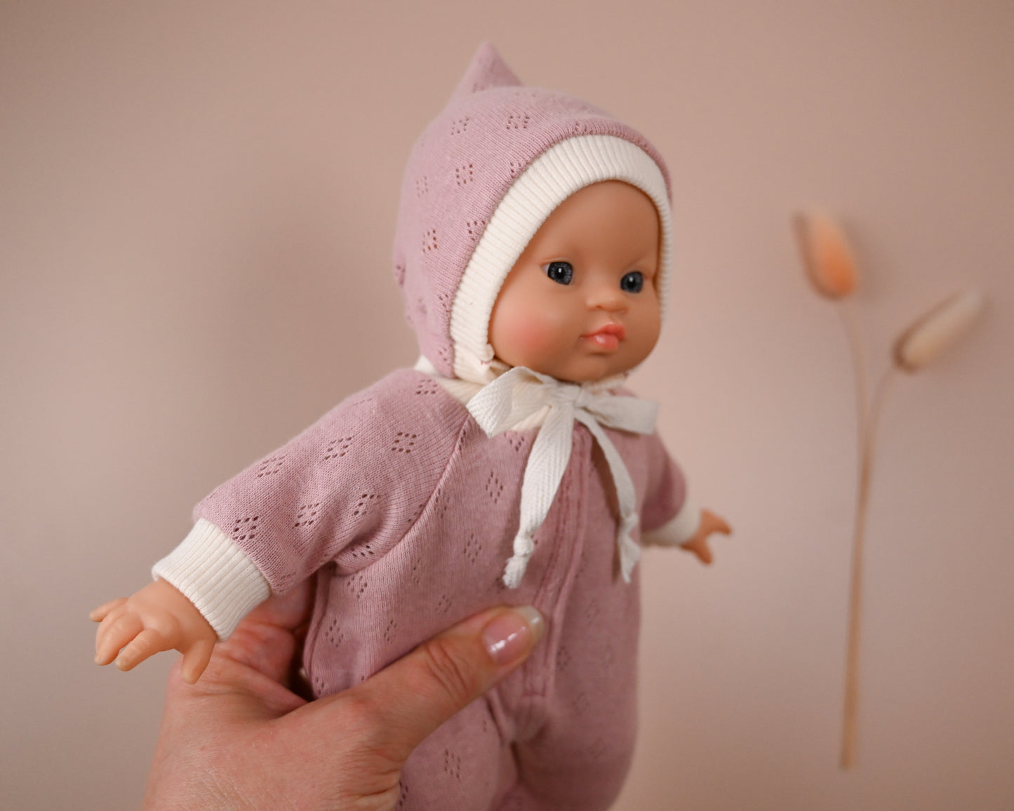 Handmade from Soft Cotton Jersey
This cosy footed sleeper is made from soft, breathable cotton jersey in a beautiful dusty rose shade — perfect for keeping your doll snug and stylish.

The delicate eyelet knit pattern adds a vintage-inspired charm, while the ribbed cuffs and matching bonnet complete the look with comfort and care. Thoughtfully designed to fit 28cm dolls like Minikane, it’s ideal for bedtime play and quiet cuddles.