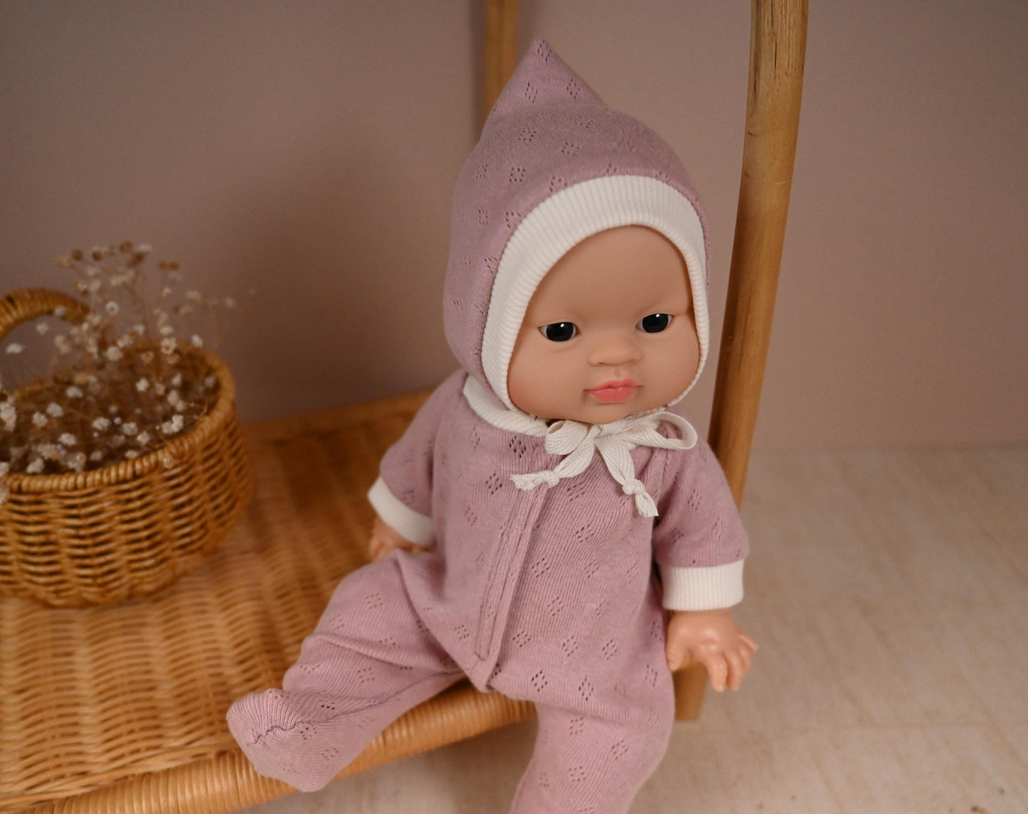 This cosy footed sleeper is made from soft, breathable cotton jersey in a beautiful dusty rose shade — perfect for keeping your doll snug and stylish.

The delicate eyelet knit pattern adds a vintage-inspired charm, while the ribbed cuffs and matching bonnet complete the look with comfort and care. Thoughtfully designed to fit 34cm dolls like Minikane and Paola Reina, it’s ideal for bedtime play and quiet cuddles.
Handmade from&nbsp; 100% Pointelle Cotton Jersey