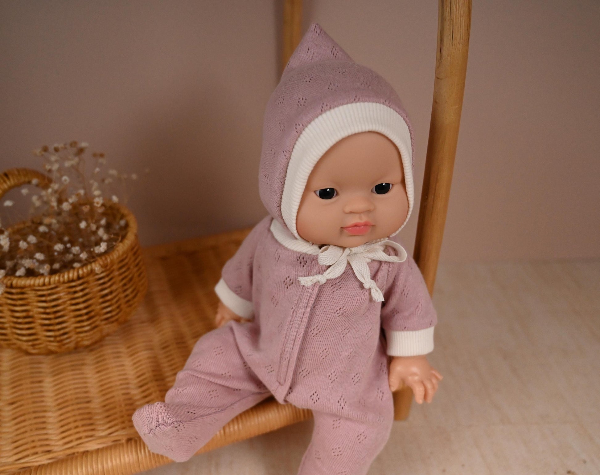 This cosy footed sleeper is made from soft, breathable cotton jersey in a beautiful dusty rose shade — perfect for keeping your doll snug and stylish.

The delicate eyelet knit pattern adds a vintage-inspired charm, while the ribbed cuffs and matching bonnet complete the look with comfort and care. Thoughtfully designed to fit 34cm dolls like Minikane and Paola Reina, it’s ideal for bedtime play and quiet cuddles.
Handmade from&nbsp; 100% Pointelle Cotton Jersey