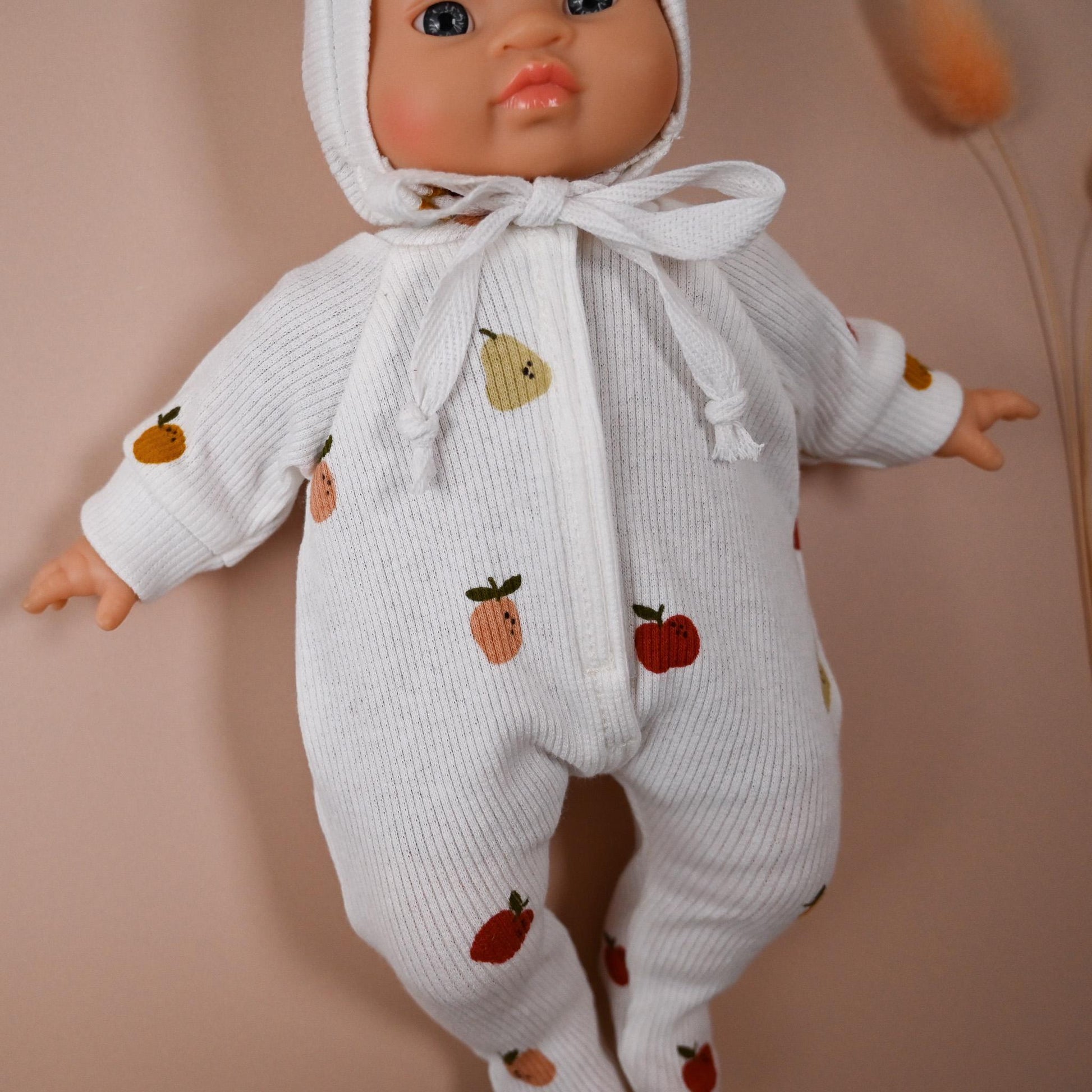 This cosy footed romper is made from soft, ribbed cotton jersey and sprinkled with colourful fruit illustrations – apples and pears&nbsp; on a creamy white background. It comes with a matching bonnet, making it perfect for naps, cuddles, or market day adventures.

Handmade from 100% cotton ribbed jersey

Fits Minikane 28cm dolls

Soft, simple, and stitched with care — perfect for dreamy doll moments.